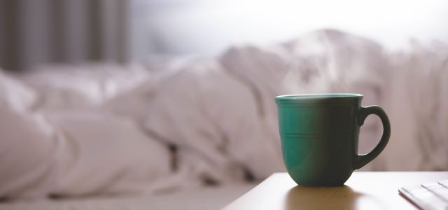 A cup of coffee on a table in front of a bed in the background