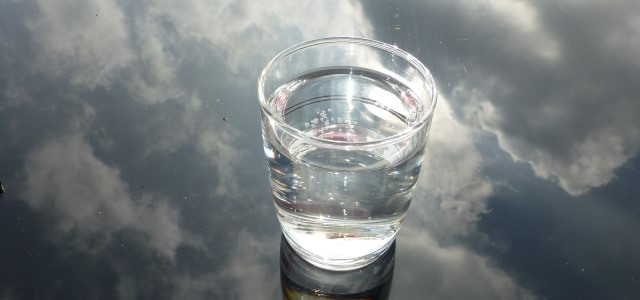 A full glass of water on a surface reflecting an image of the sky